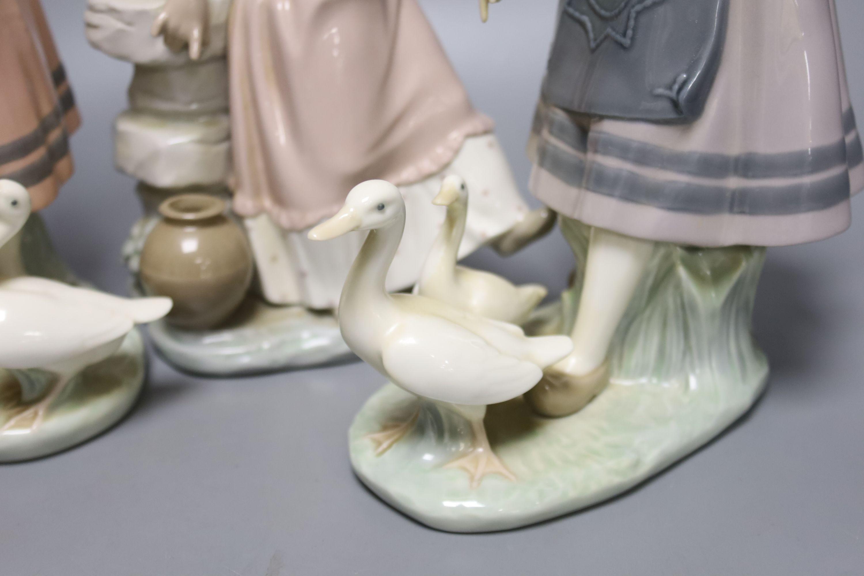 A Lladro figure of a girl feeding a duck, another sitting on a wall, and a girl with two ducks, tallest 26cm